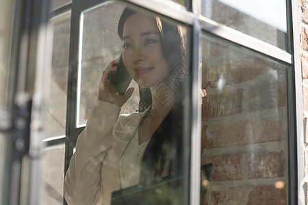 窗边接听电话的青年女子背景图片