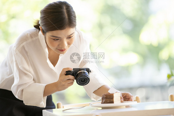 拿着相机拍甜品照片的年轻女子图片