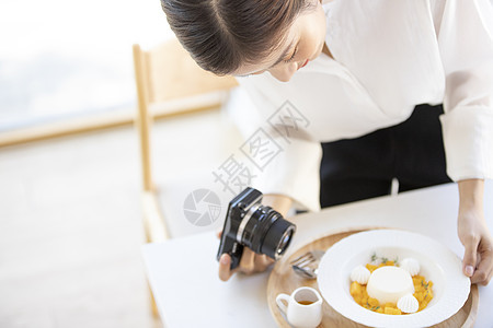 年轻女子拿着相机拍摄食物照片图片