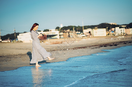 海边拿着相机漫步的年轻女子图片