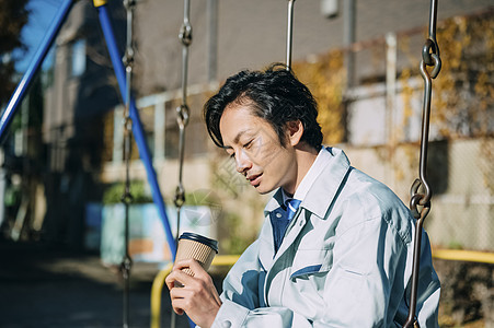 坐在公园秋千上喝咖啡的男性职员图片