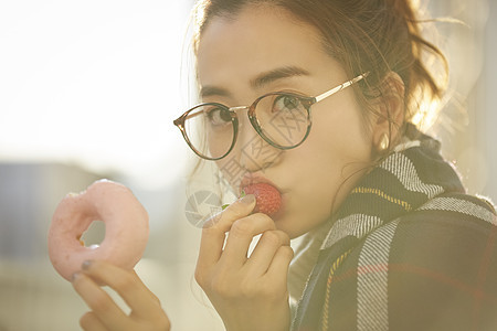 拿着甜甜圈吃草莓的年轻女子图片