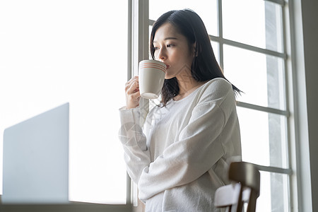 站在窗边喝咖啡思考的年轻女子图片