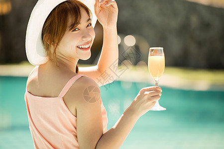 年轻女子在游泳池旁喝果汁享受度假图片
