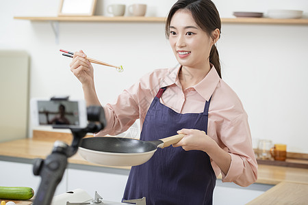 拍摄烹饪做菜短视频的年轻女子背景图片