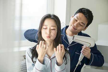 丈夫拿着吹风机给妻子吹头发图片素材