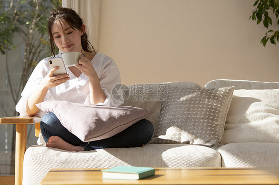 坐在沙发上喝咖啡看手机的年轻女子图片
