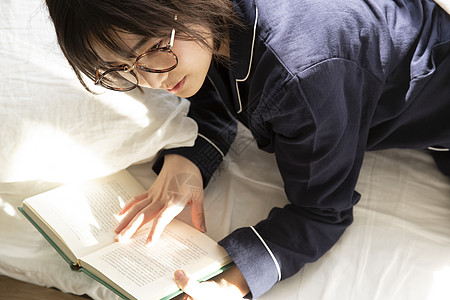 床上翻开书阅读的年轻女子背景图片