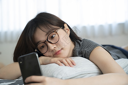 趴在床上玩手机的年轻女子图片素材