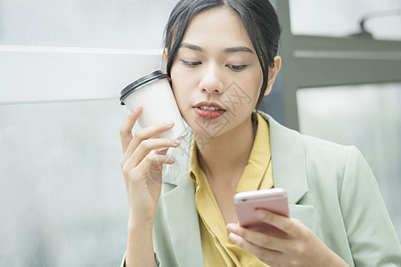 拿着咖啡看手机的青年商务女性图片