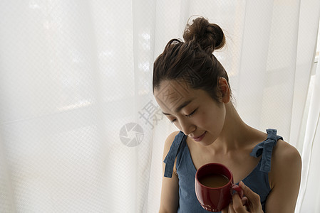 窗边拿着咖啡的青年女性图片