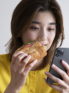 吃三明治看手机的年轻女子图片