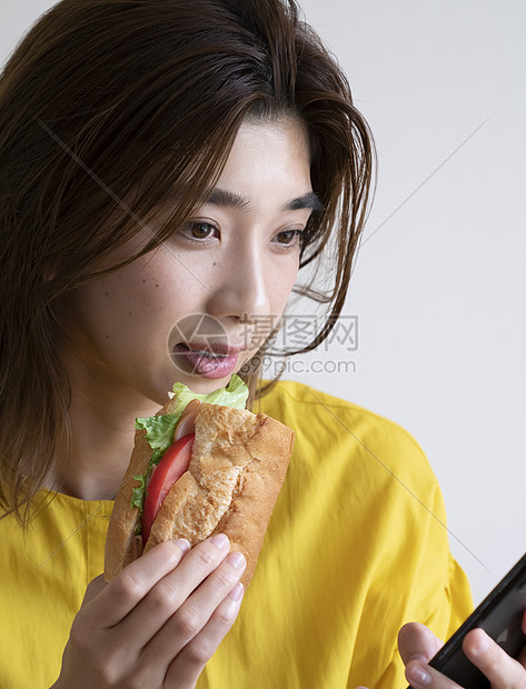 拿着三明治看手机的年轻女子图片