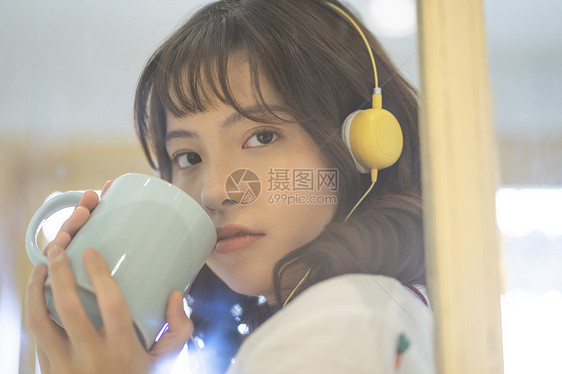 戴着耳机喝水的年轻女子图片