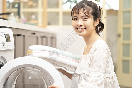 年轻女子将衣物毛巾放进洗衣机图片