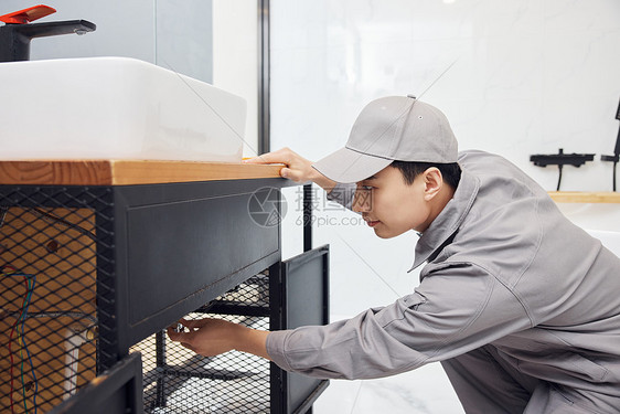 男性维修工检修洗手盆下水管图片