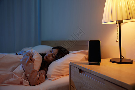 居家女性卧室睡觉和床头柜上的手机图片