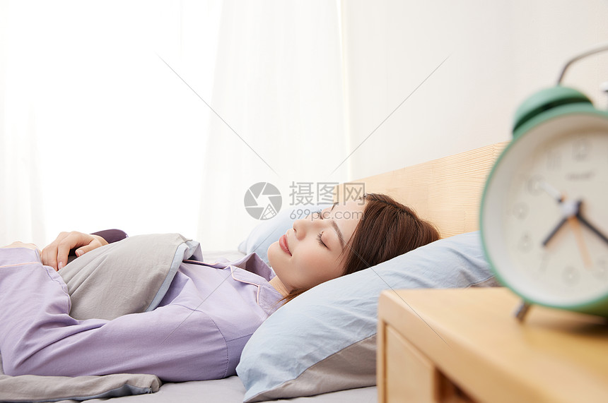 睡觉的年轻女性和床头柜上的闹钟图片
