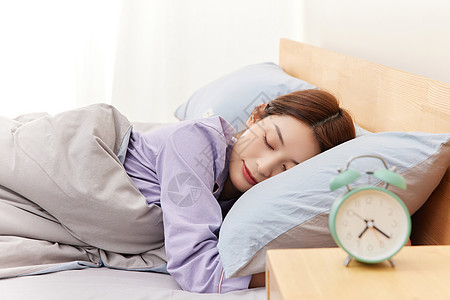 睡觉的年轻女性和床头柜上的闹钟高清图片