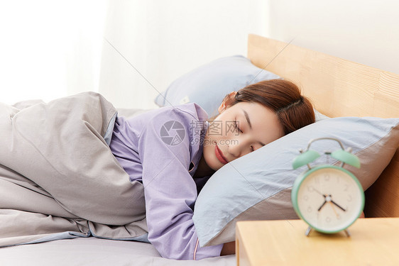 睡觉的年轻女性和床头柜上的闹钟图片