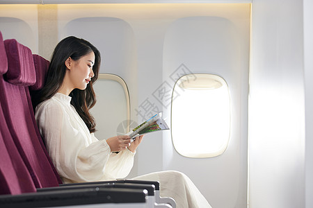 商务飞机年轻美女飞机上翻阅杂志背景