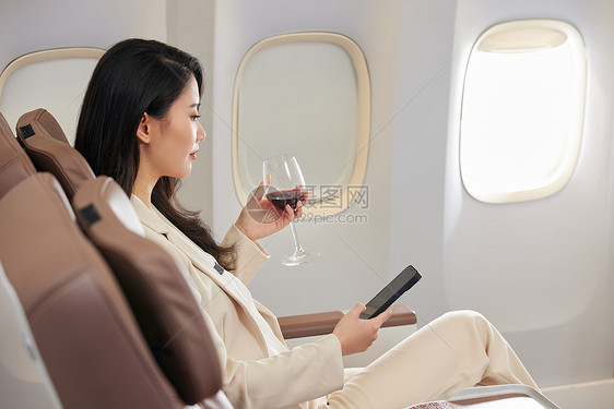 在头等舱里品尝红酒的年轻商务女士图片