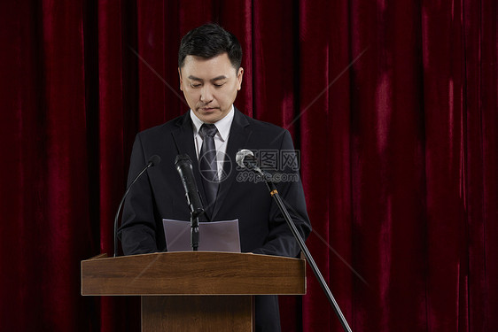 商务男士舞台上拿着演讲稿发言图片