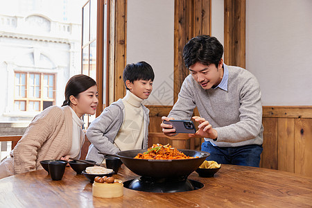 火锅店吃火锅的幸福家庭拿手机拍照记录图片