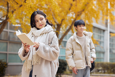 银杏树下手拿书本的年轻大学生图片