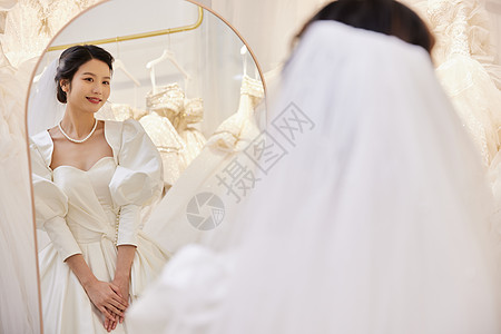 穿着婚纱站在试衣镜前的女性图片