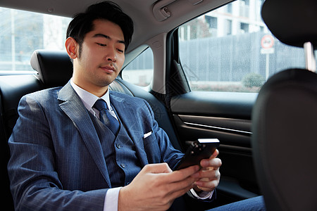 商务男性乘客坐在车里看手机图片