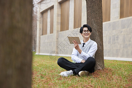 青年男性学生坐草地上学习图片