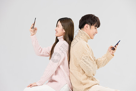 韩系情侣背靠背看手机背景图片