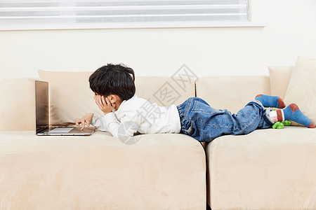 小朋友趴在沙发上玩耍看电脑图片