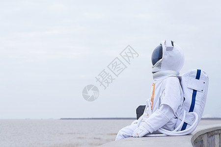 户外穿着宇航服坐在海边的男性图片