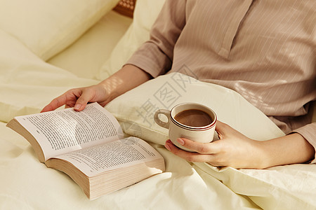 卧床看书喝咖啡的女性手部特写图片