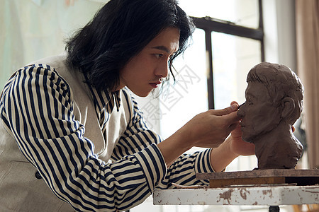 男青年专注雕刻泥塑作品图片