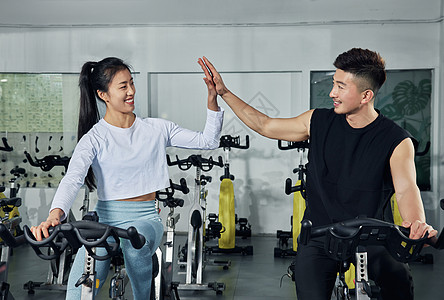 健身房动感单车训练的健身男女击掌鼓励图片
