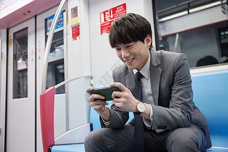 在地铁上玩手机的商务男性图片