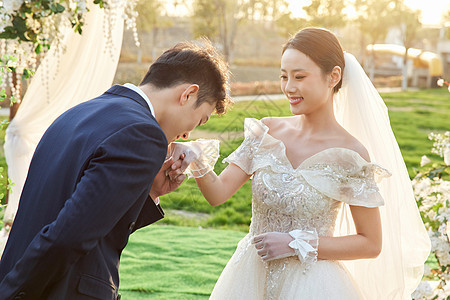 举行户外婚礼的新郎亲吻新娘的手背背景图片