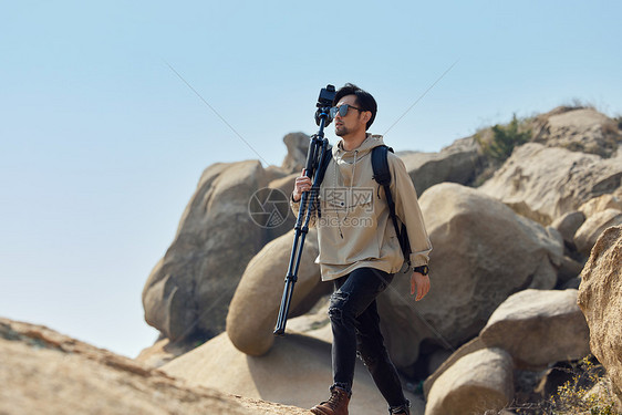 户外登山的摄影师扛三脚架堪景图片