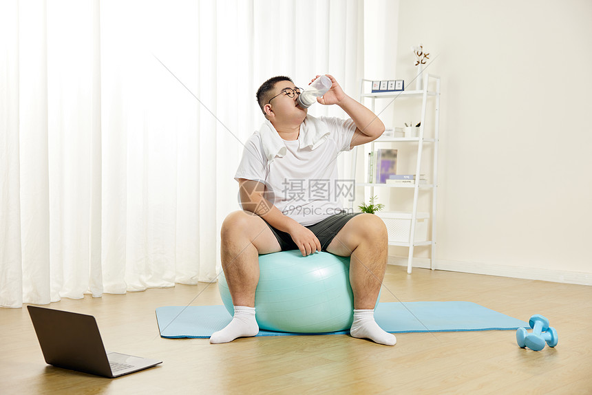 肥胖男士瑜伽球上喝水休息图片
