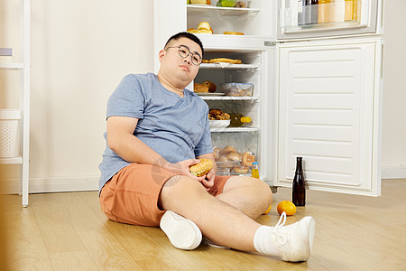 贪吃的肥胖男青年坐在冰箱旁图片