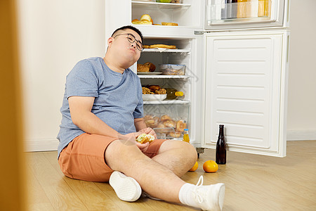 贪吃的肥胖男士坐在冰箱旁图片