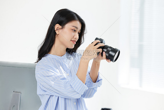 青年女摄影师手拿相机拍摄照片图片