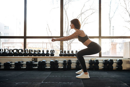 女运动员站和做蹲在健身房图片