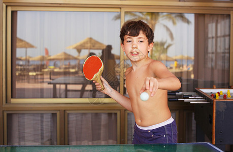 青春期前帅气的男孩打乒乓球在海滩度假村酒店图片