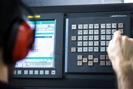 Cnc操作员机械技师在金属加工铣削中心与键盘戴降噪耳机插入数据的工具车间工人图片