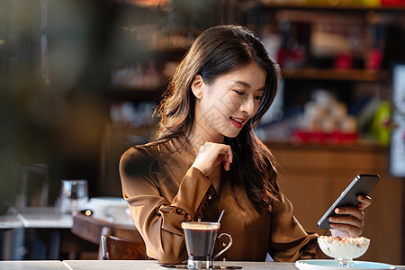 咖啡馆内边喝咖啡边使用手机的青年女人图片