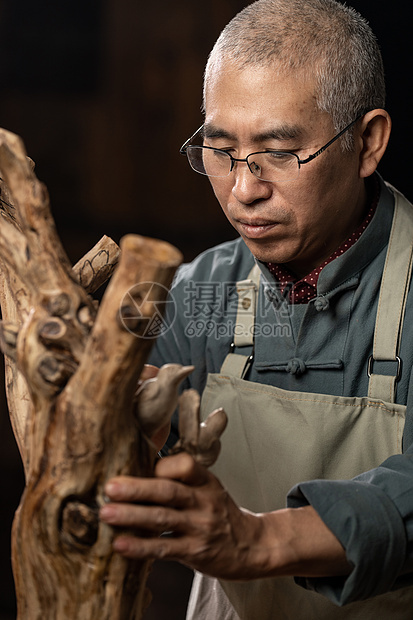 在树根上认真雕刻的工匠师图片